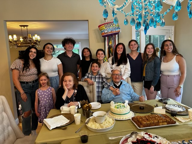 A photo of the family by a table filled with desert and cake to celebrate Naim's birthday. The family and grandkids are smiling.